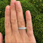 Hand wearing a platinum ring with 9 emerald cut diamonds  a green grass background