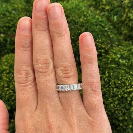 Hand wearing a platinum ring with 9 emerald cut diamonds  a green grass background