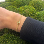 14K Gold Puff Mariner bracelet on a wrist against a green textured background