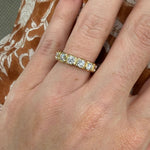 18K Gold band ring with bezel set diamonds on a woman's finger against a patterned fabric background