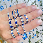 Hand wearing multiple sapphire and diamond platinum rings on a floral fabric background
