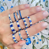 Hand wearing multiple sapphire and diamond platinum rings on a floral fabric background