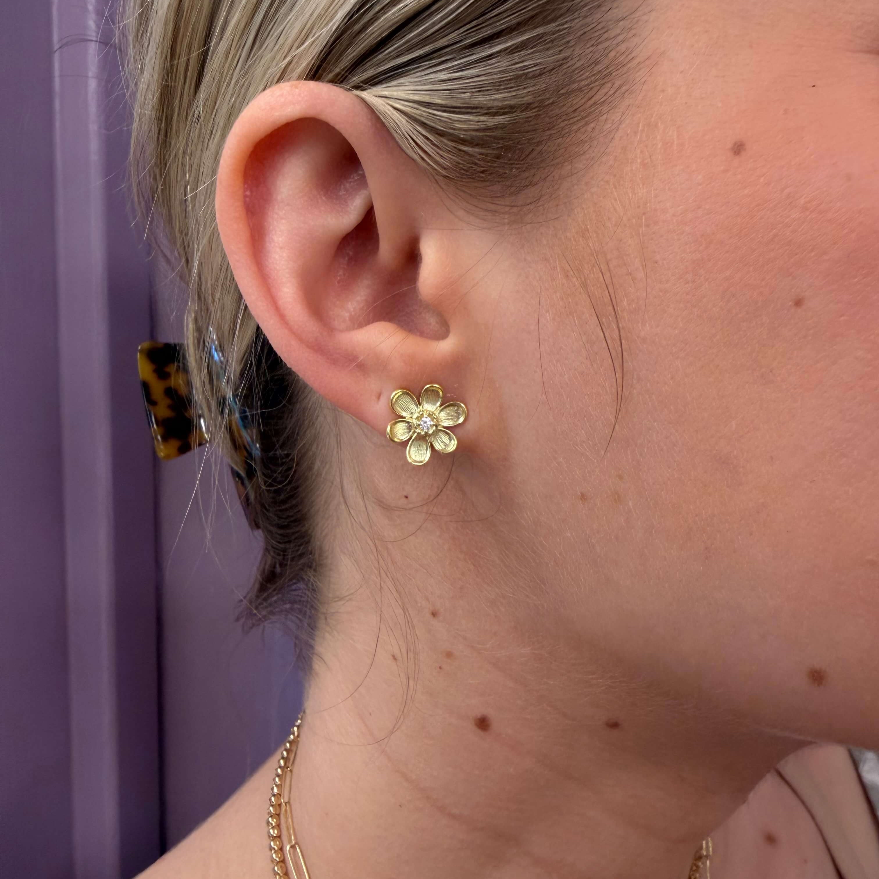 Close-up of a person wearing a gold earring with a floral design.