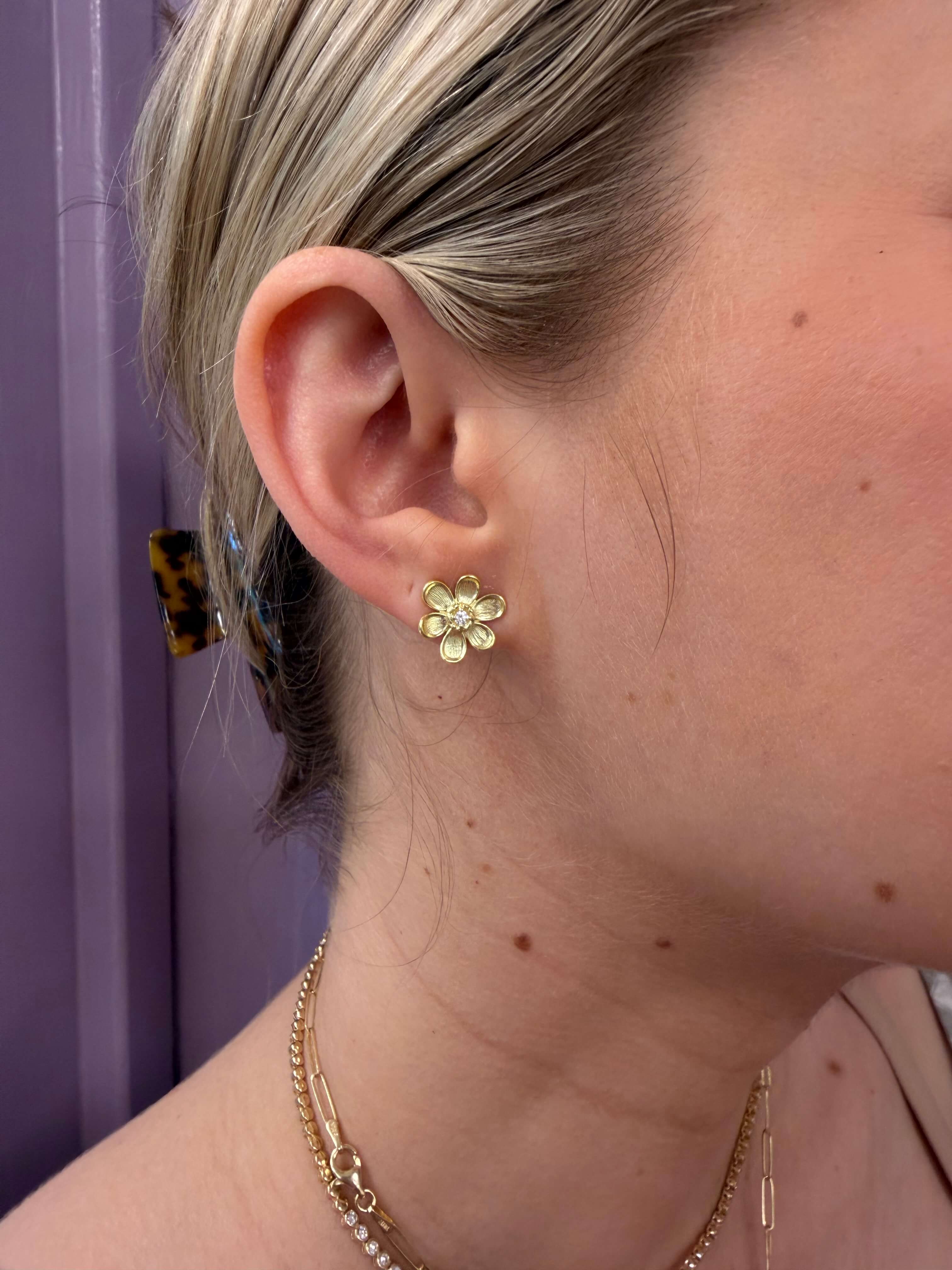 Close-up of a person wearing a gold earring with a floral design.