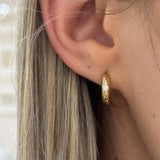 Close-up of a gold hoop earring worn by a person with blonde hair.