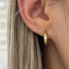 Close-up of a gold hoop earring worn by a person with blonde hair.