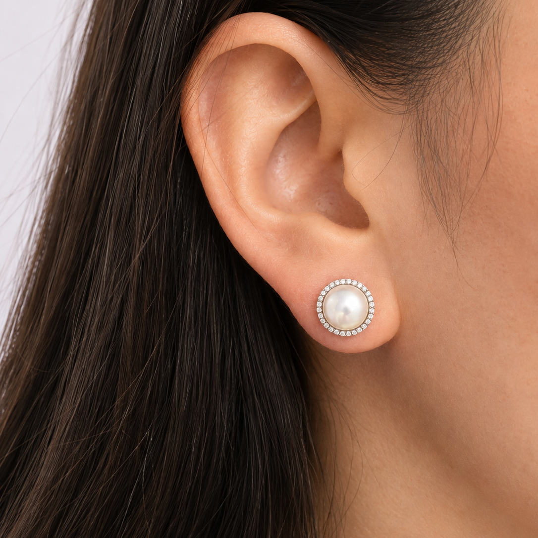 A close-up of a model's ear wearing a stud earring with a central white pearl surrounded by a halo of diamonds