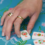 Hand with 14K gold diamond rings on a colorful surface with game pieces