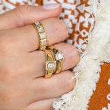 Gold rings with diamonds on a hand against an orange and white patterned fabric background