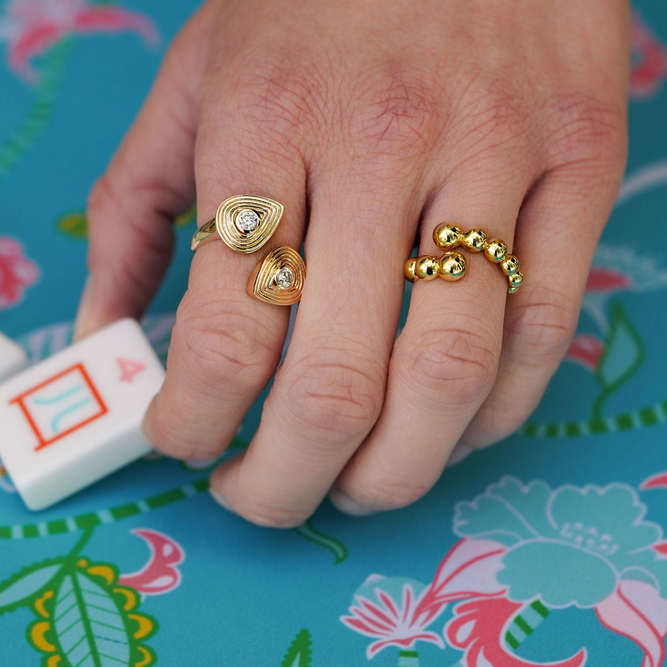 Hand wearing 14K gold rings on a colorful tablecloth with mahjong game pieces.