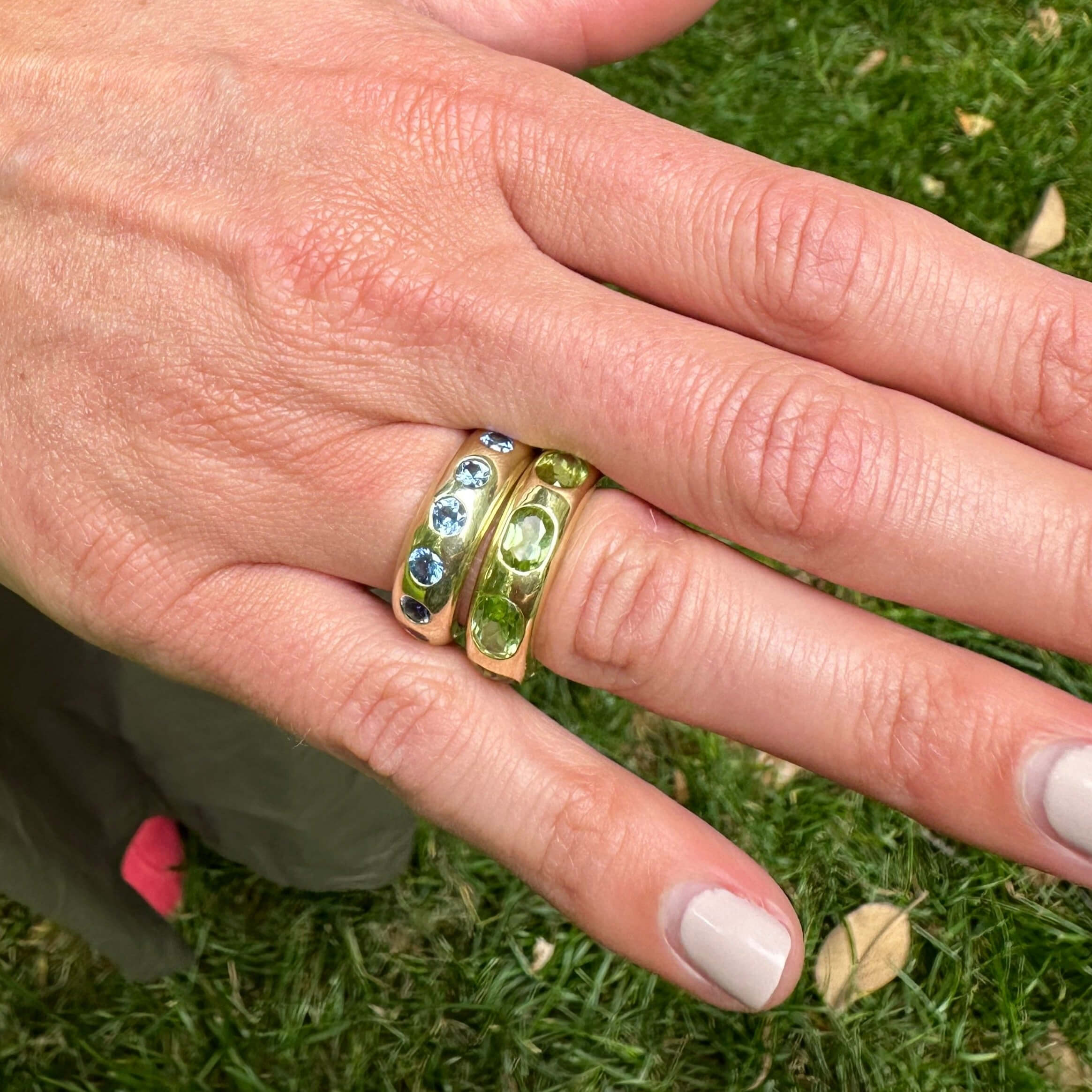 Hand wearing a 14K gold ring with gemstones against a grass background