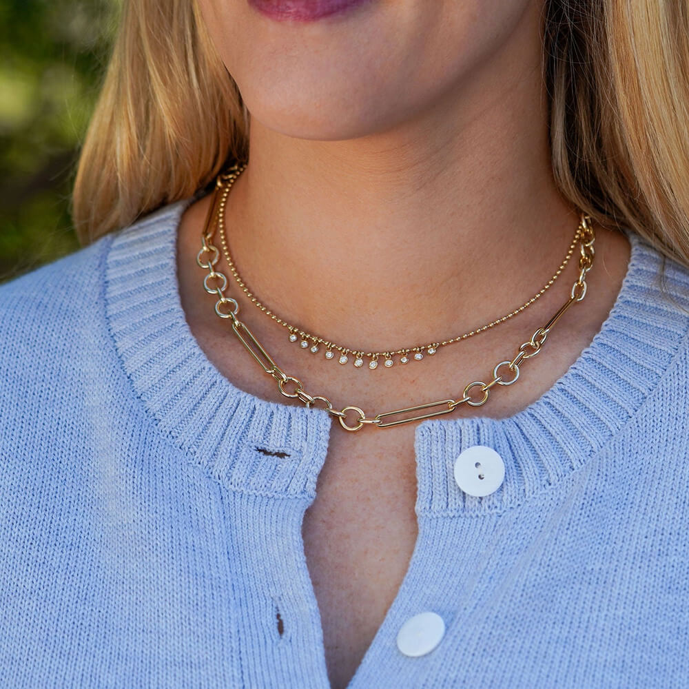 Close-up of a person wearing a gold necklace with a blurred natural background