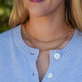 Close-up of a person wearing a gold necklace with a blurred natural background