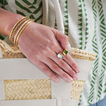 Close-up of a hand with gold bangles and a ring, holding a woven bag.