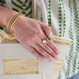 Close-up of a hand with gold bangles and a ring, holding a woven bag.