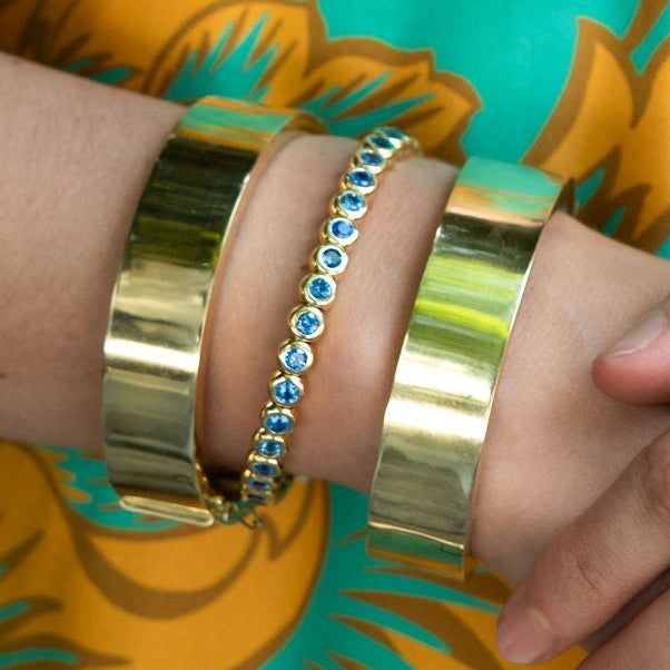 Close-up of hands with gold bracelets and a ring against a floral-patterned fabric background.
