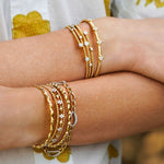 Close-up of woman wearing multiple gold bracelets and rings on a blurred natural background