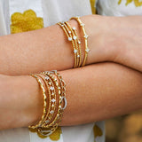 Close-up of woman wearing multiple gold bracelets and rings on a blurred natural background