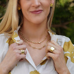 Woman wearing gold jewelry outdoors with greenery in the background