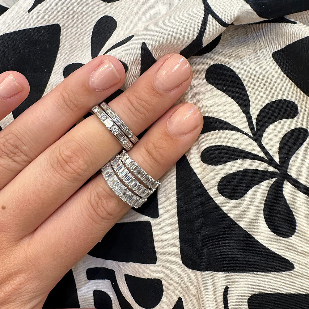 Hand wearing multiple platinum and diamond rings with a black and white patterned fabric background