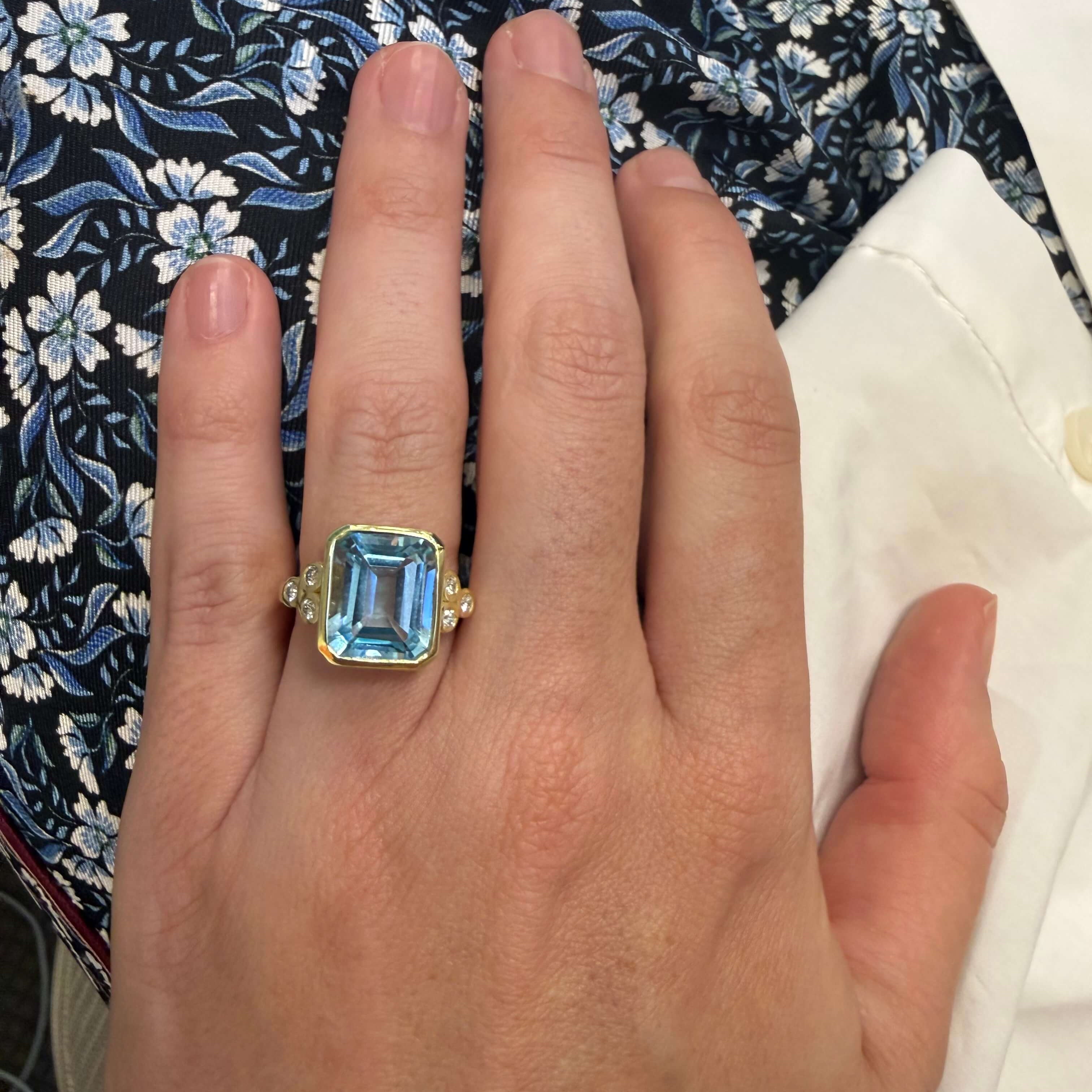 Hand wearing a ring with a blue gemstone against a floral fabric background