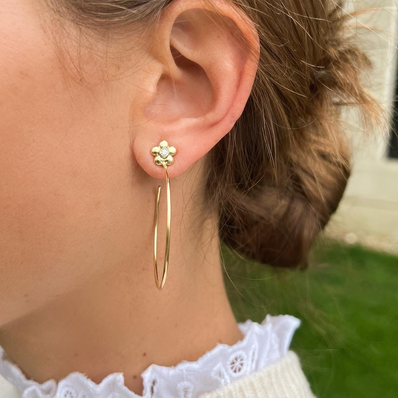 woman wearing 18K gold hoop earrings with single diamond in center of flower design on stud