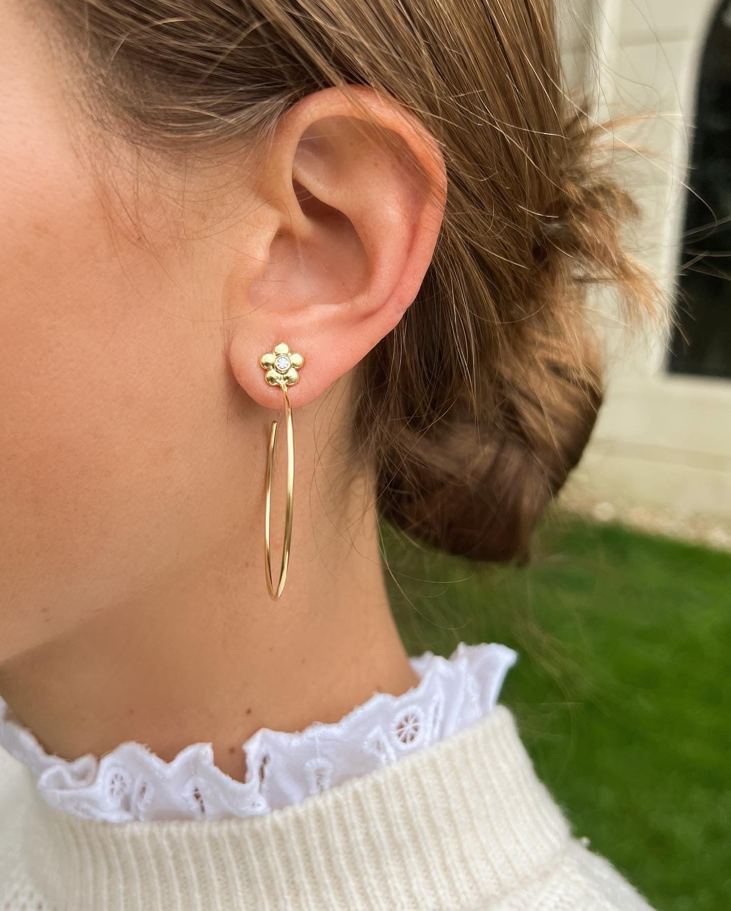 woman wearing 18K gold hoop earrings with single diamond in center of flower design on stud
