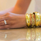Woman wearing several 18K yellow gold bracelets designed by Laura Pearce