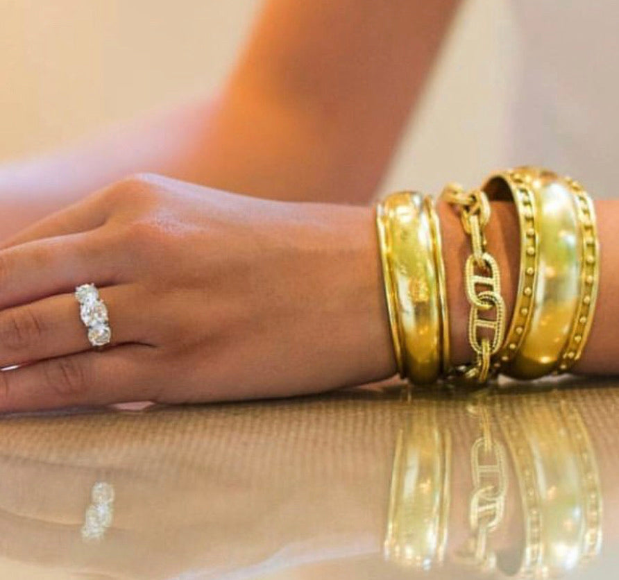Woman wearing several 18K yellow gold bracelets designed by Laura Pearce