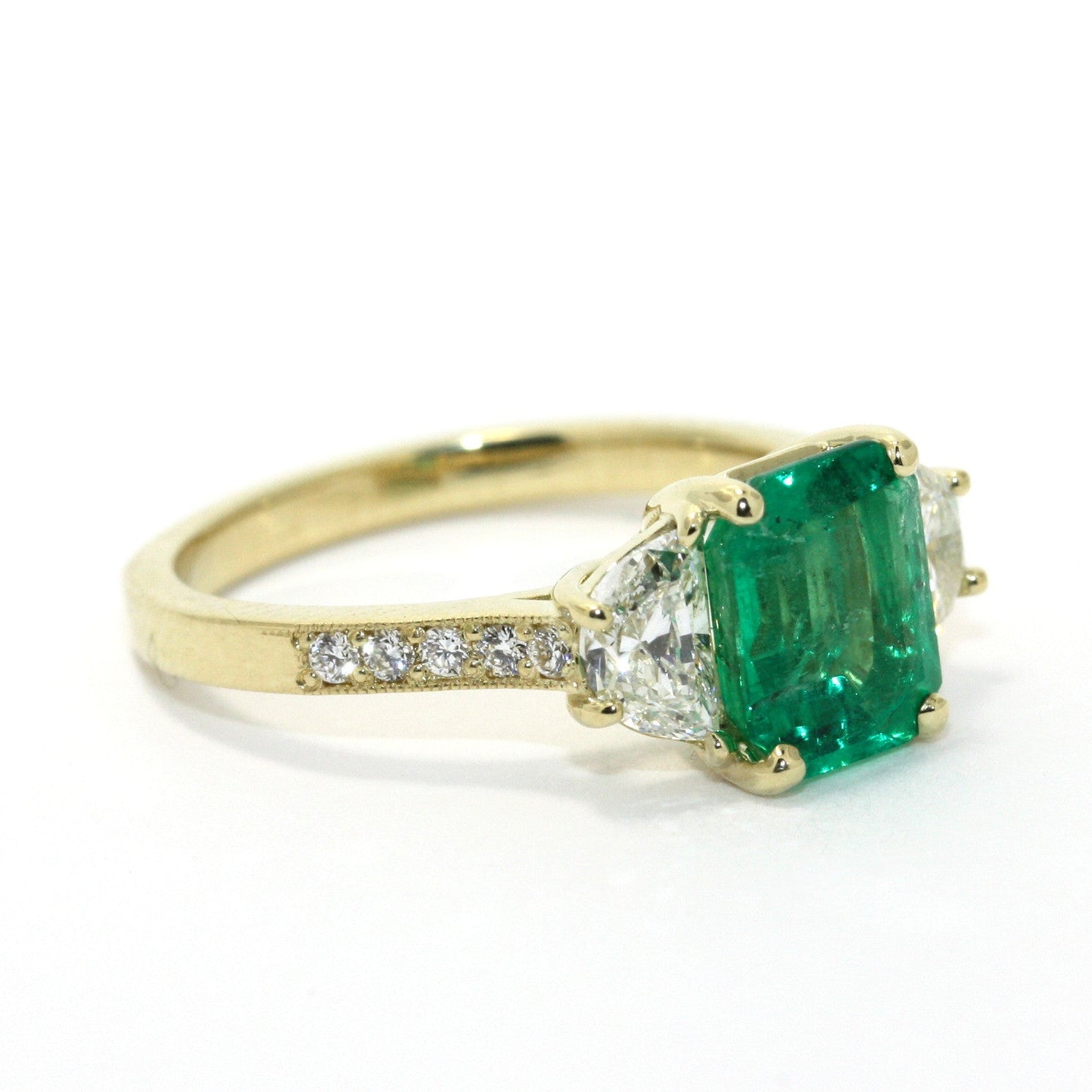 An 18K yellow gold ring featuring a central emerald stone and two smaller half moon diamonds.