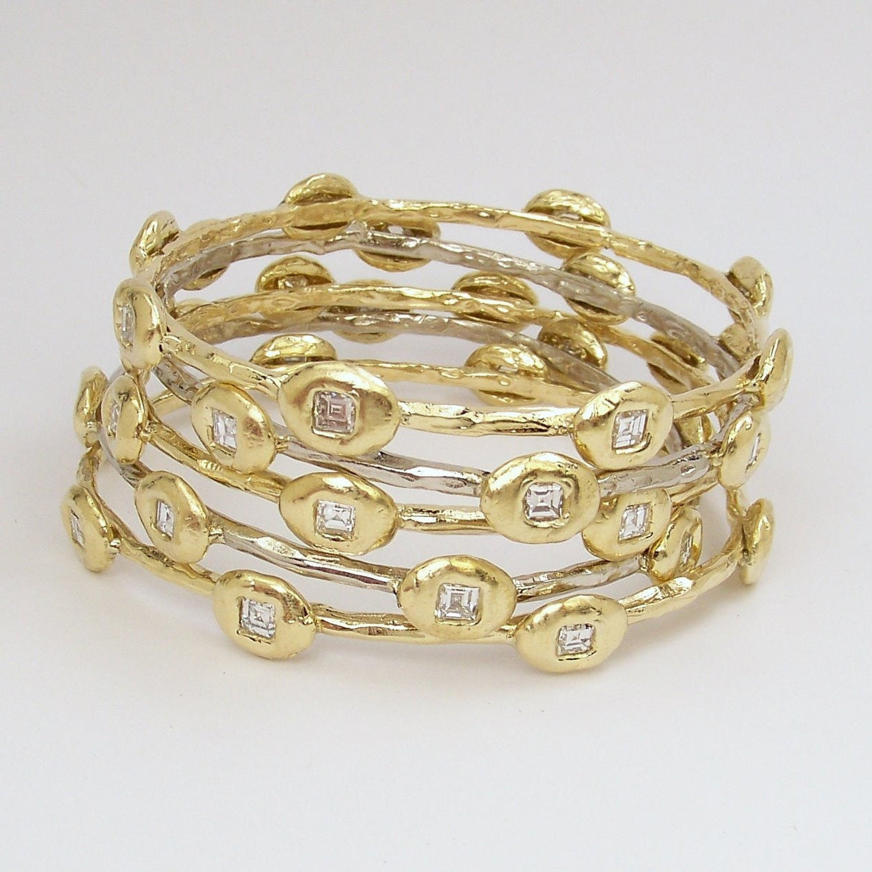 A series of stackable 18K yellow gold bangle bracelets, featuring a chain of diamonds.