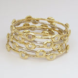 A series of stackable 18K yellow gold bangle bracelets, featuring a chain of diamonds.