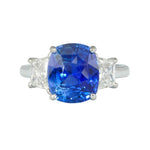 A custom designed platinum cushion cut sapphire and diamond ring with a large blue sapphire surrounded by smaller diamonds.