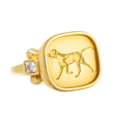 An 18k yellow gold ring featuring a large square top with an engraved image of a dog and a small diamond on the side.