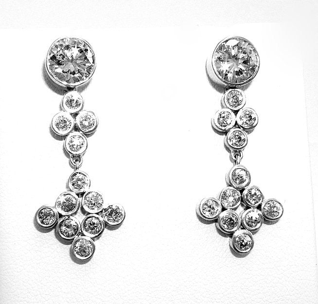 A pair of platinum diamond bezel set drop earrings displayed on a white surface.