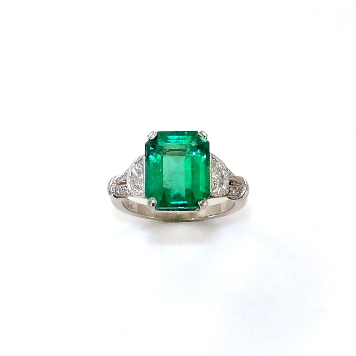 A platinum ring with a central emerald gemstone and two smaller diamonds set in a classic prong setting.