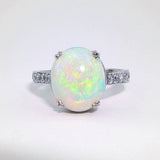 A platinum ring with a central opal stone and smaller diamonds around the band.