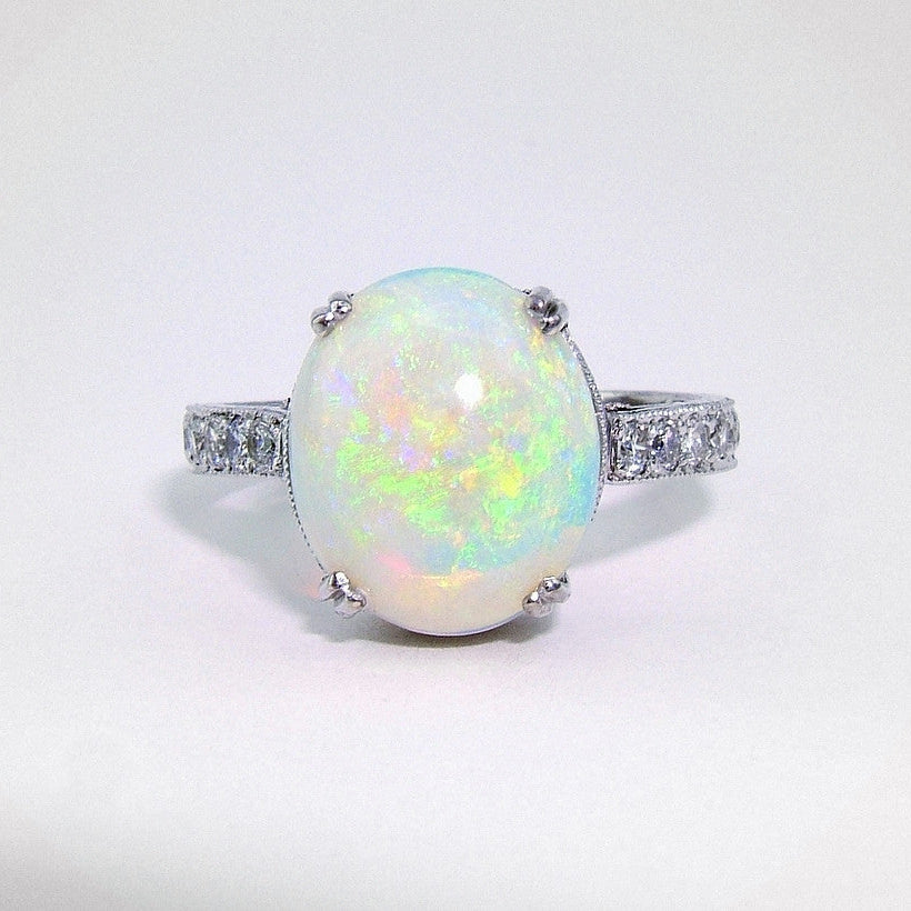 A platinum ring with a central opal stone and smaller diamonds around the band.