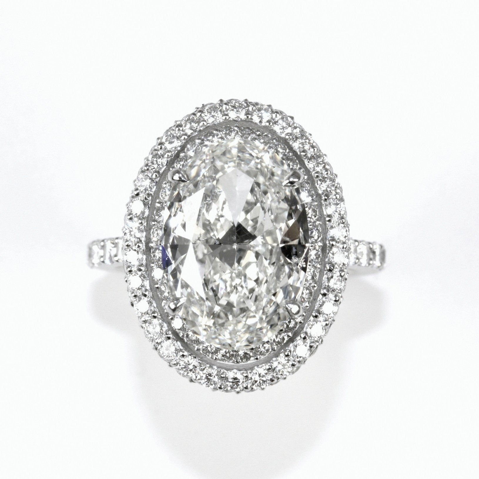 A platinum oval diamond halo ring with a clear, center diamond surrounded by smaller diamonds set in an oval pattern.