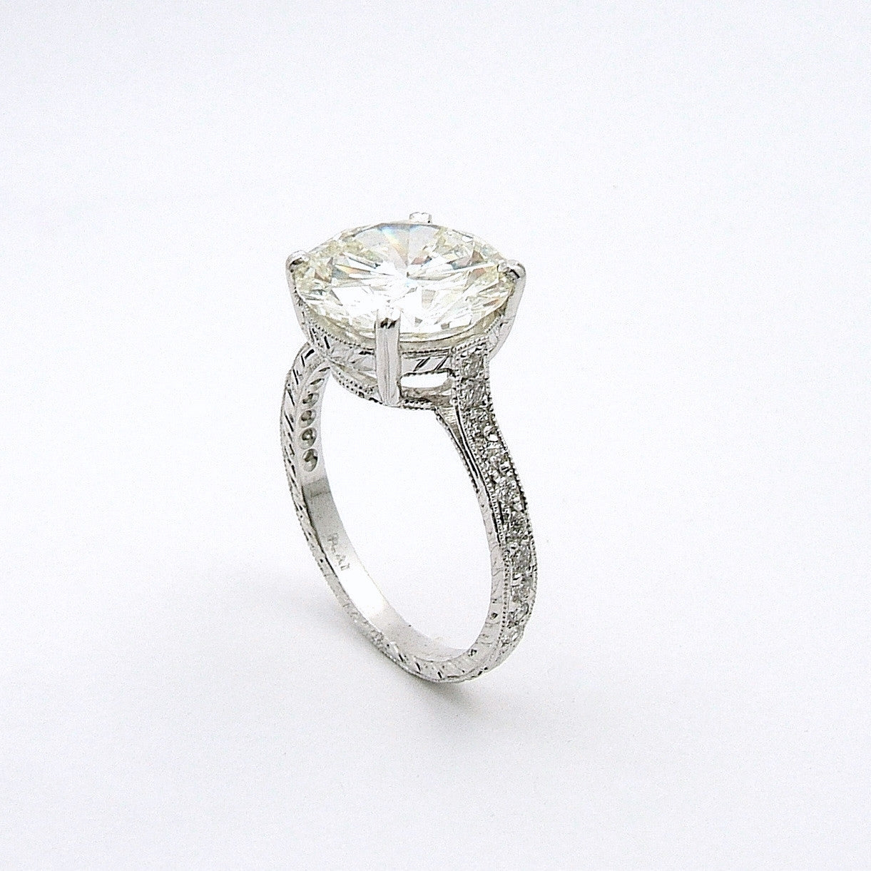 A platinum round diamond engagement ring with a filigree band and a round diamond top.
