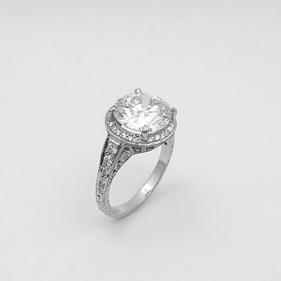 A platinum round diamond ring with a halo effect, featuring smaller round diamonds set along the band.