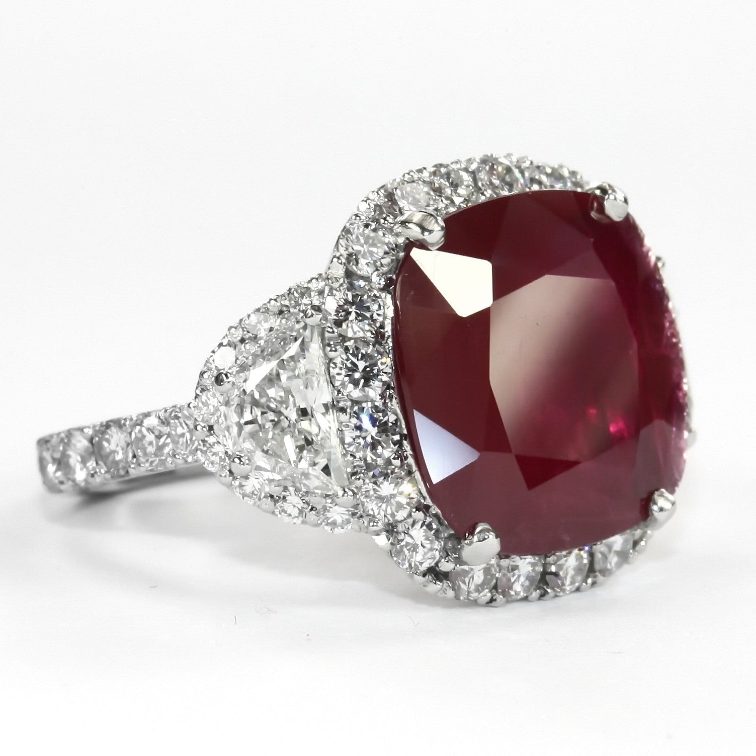 A ring with a large red ruby center stone, flanked by two half-moon shaped diamonds on a platinum band.