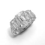 A platinum three-stone emerald cut diamond ring with a round diamond halo